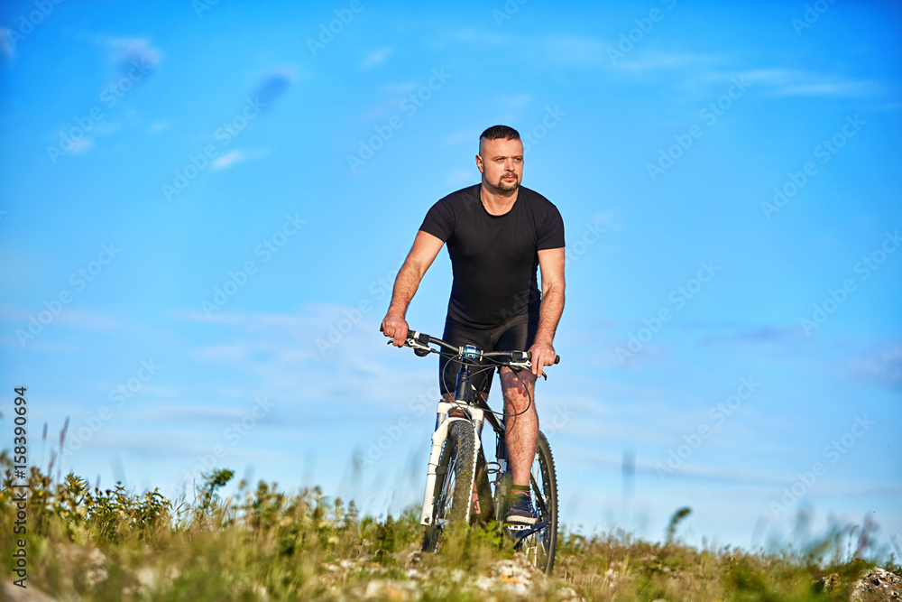 Young man cycling on a green meadow against blue sky with clouds. Young man cycling on a green meadow against blue sky with clouds.