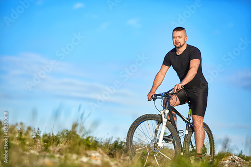 Fototapeta Naklejka Na Ścianę i Meble -  Young man cycling on a green meadow against blue sky with clouds.