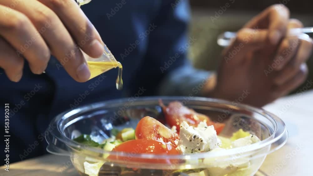 Close up of man s hand adding oil from a small plastic container to his Greek salad in a cafe. Handheld real time close up shot Close up of man s hand adding oil from a small plastic container to his Greek salad in a cafe. Handheld real time close up shot