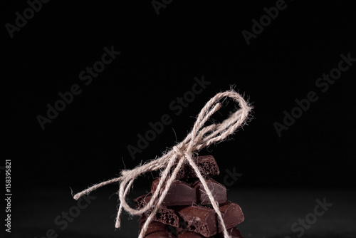 A stack of black pore chocolate tied with twine thread from twine on a black background