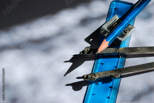 A compass, ruler, crayon and metal sharpener between the shadows and lights