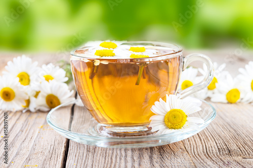 cup of camomile tea and camomile flowers on wooden background