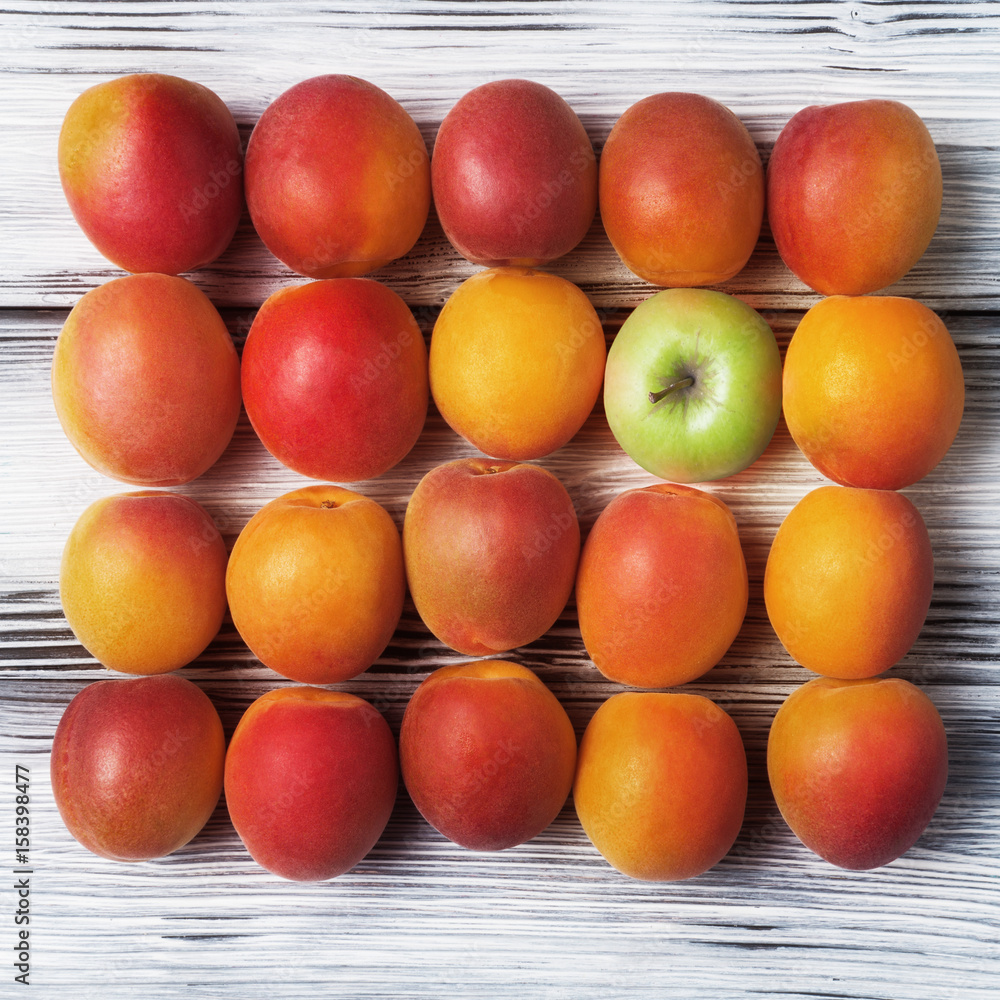 Ripe apricots and one apple on wooden background