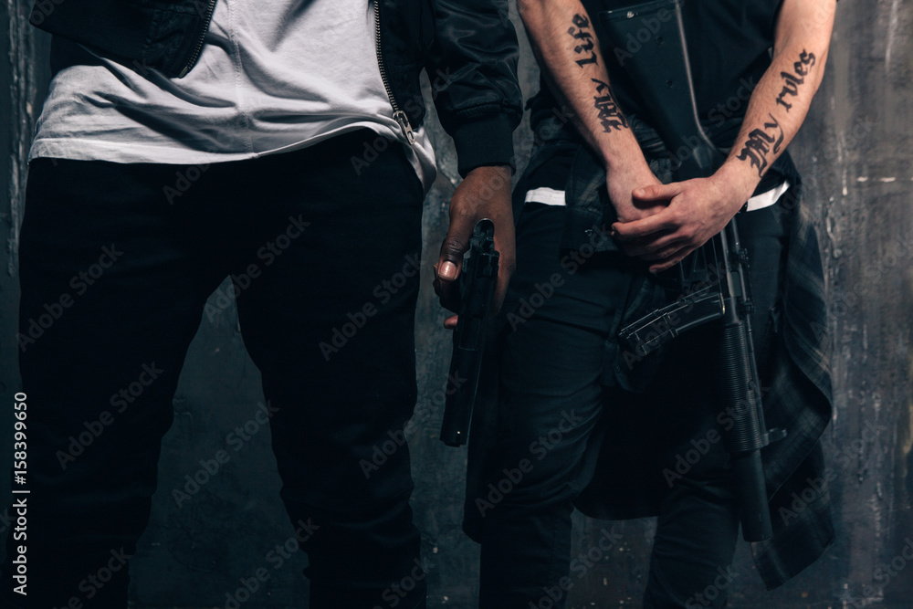 Group of unrecognizable criminals with guns. Armed gangsters with tattoo on dark background. Outlaw, ghetto, murderer, robbery concept Group of unrecognizable criminals with guns. Armed gangsters with tattoo on dark background. Outlaw, ghetto, murderer, robbery concept
