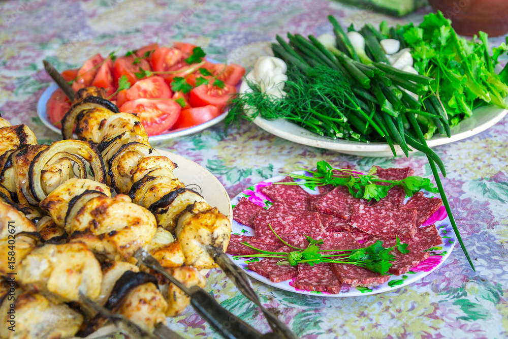 On the table plates with shish kebabs, sausage, greens and vegetables. Picnic. Food on the table On the table plates with shish kebabs, sausage, greens and vegetables. Picnic. Food on the table
