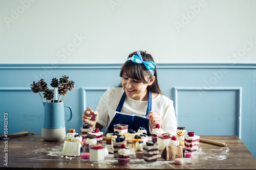 Photos Young beautiful woman in an apron making cake with cream and berries at the kitc