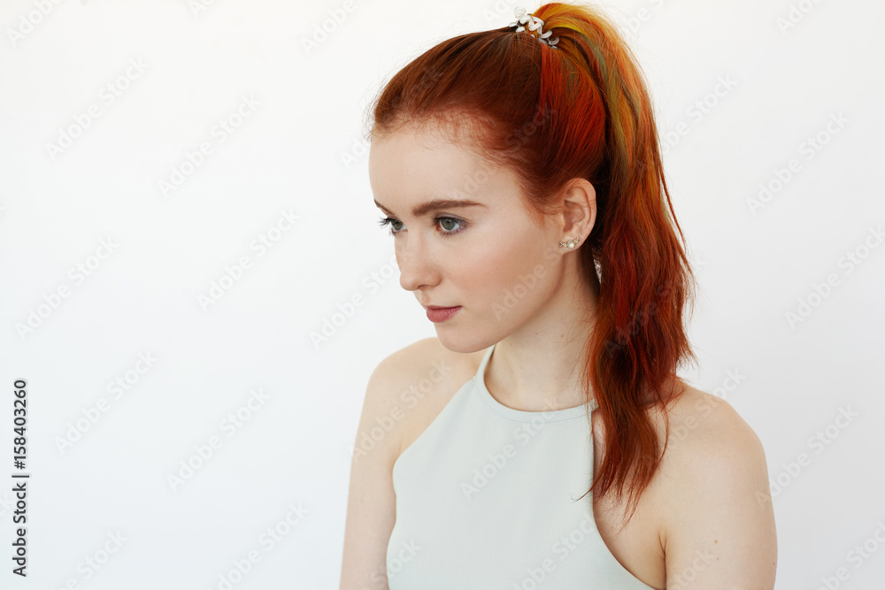 Side view on handsome redhead teenage girl with multi-coloured strand in  hair. Hipster student female with long ginger hair in ponytail and healthy  skin looking aside. Youth, beauty and fashion trends Stock