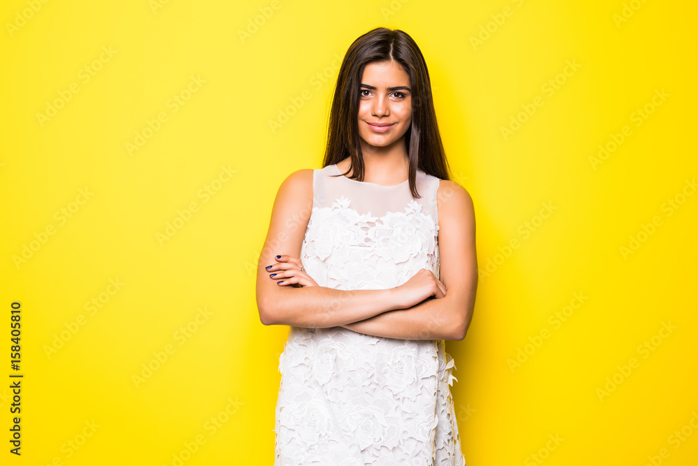 Portrait of a beautiful young woman witn crossed hands smiling on yellow background Portrait of a beautiful young woman witn crossed hands smiling on yellow background