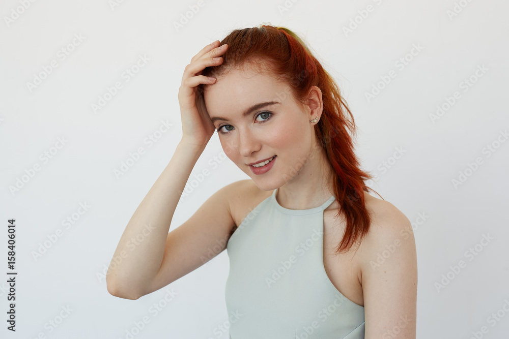 Close up view of beautiful Caucasian teenage woman smiling joyfully tying her long red hair in ponytail. Young Caucasian female model looking at camera posing on white background. Youth and happiness Close up view of beautiful Caucasian teenage woman smiling joyfully tying her long red hair in ponytail. Young Caucasian female model looking at camera posing on white background. Youth and happiness