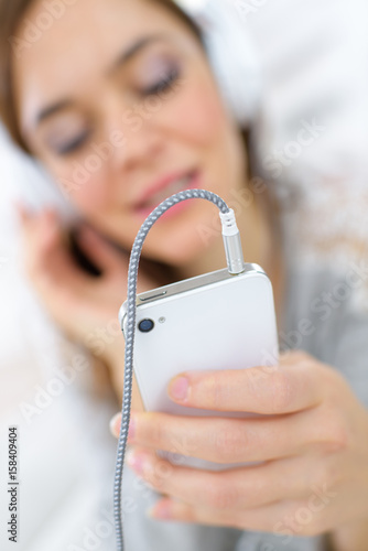 Woman listening to headphones plugged into smartphone photo