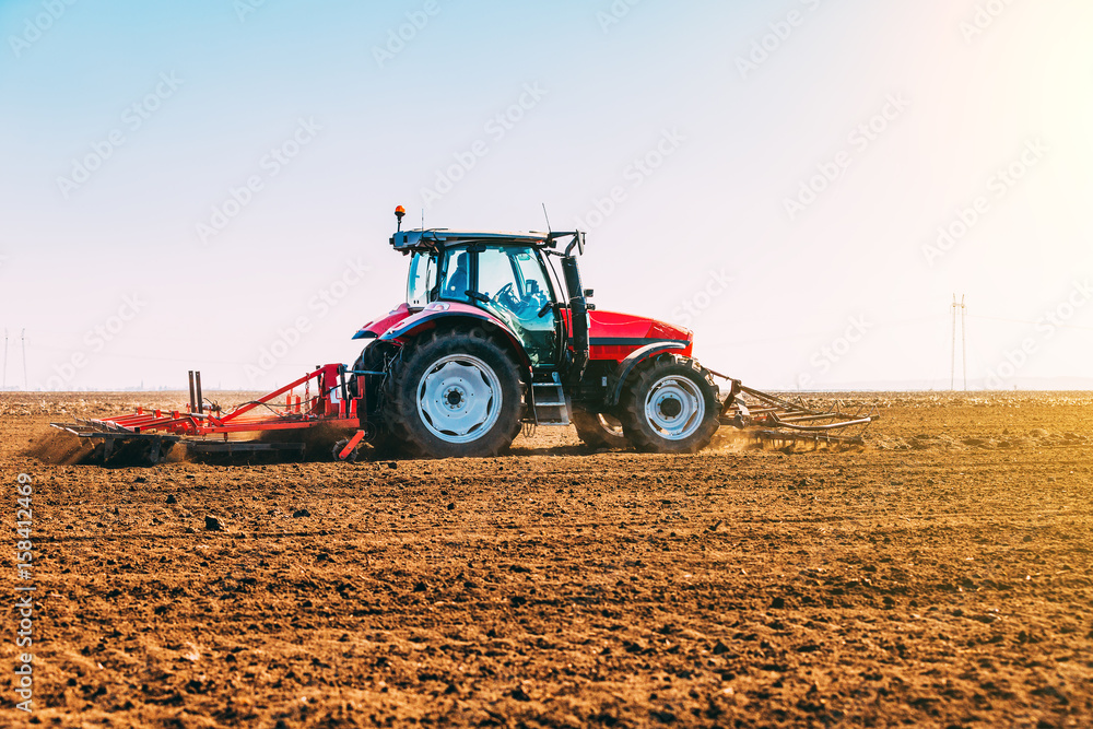 Obraz premium Farmer in tractor preparing land with seedbed cultivator as part of pre seeding activities in early spring season of agricultural works at farmlands.