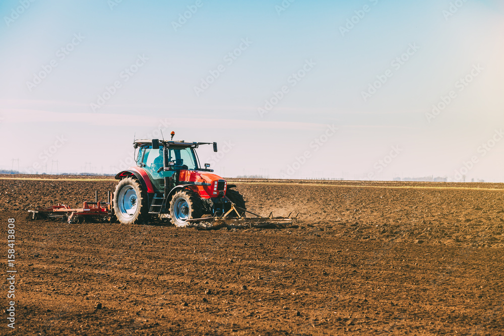 Fototapeta premium Farmer in tractor preparing land with seedbed cultivator as part of pre seeding activities in early spring season of agricultural works at farmlands.