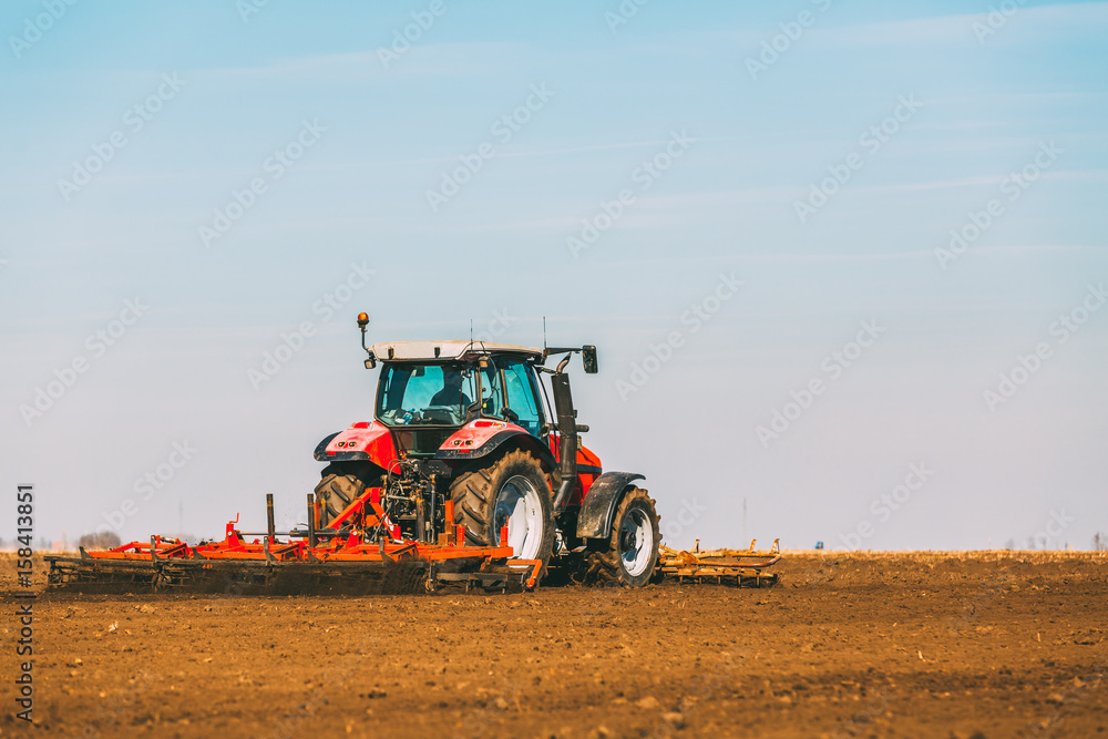 Obraz premium Farmer in tractor preparing land with seedbed cultivator as part of pre seeding activities in early spring season of agricultural works at farmlands.