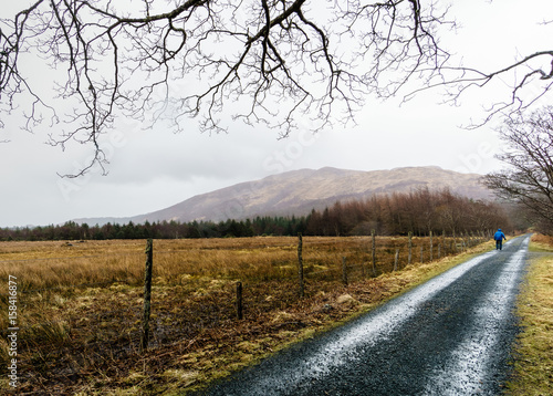 Man in Blue Coat Walking Down Gravel Path in the Countryside photo