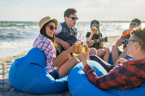 group of friends with guitar and alcohol on the beach party . Man and woman clink glasses. Cheers. Happy youth time © Igor Kardasov