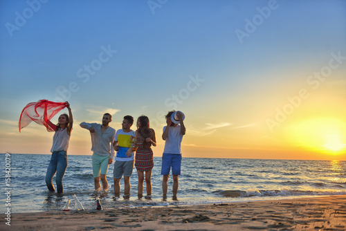 Group of happy young people is running on background of sunset beach and sea