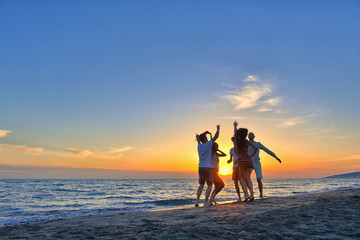 group of happy young people dancing at the beach on beautiful summer sunset