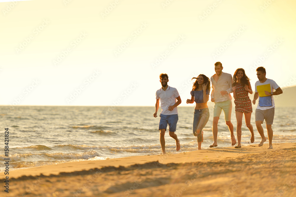 Group of friends having fun walking down the beach at sunset