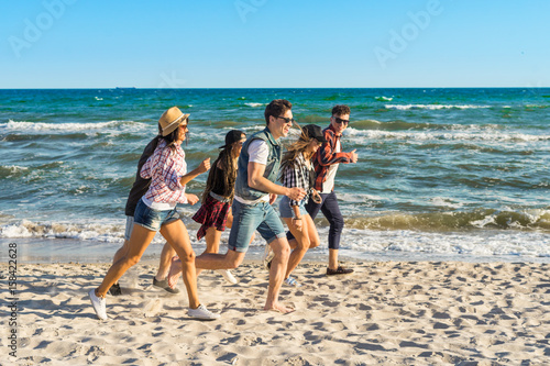 Group of hipster young friends running along beach together. Sea is on background © Igor Kardasov