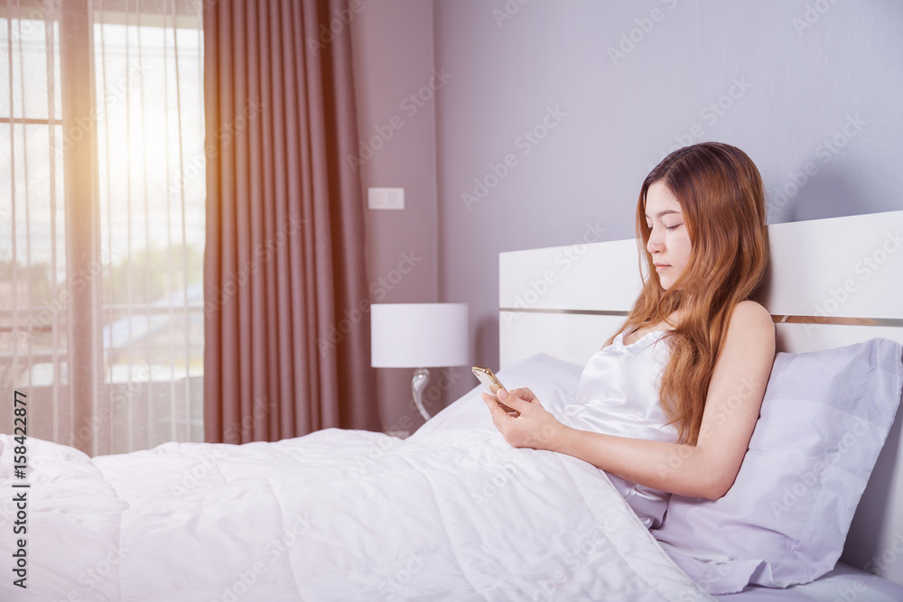 woman using her smartphone on bed in bedroom with soft light woman using her smartphone on bed in bedroom with soft light