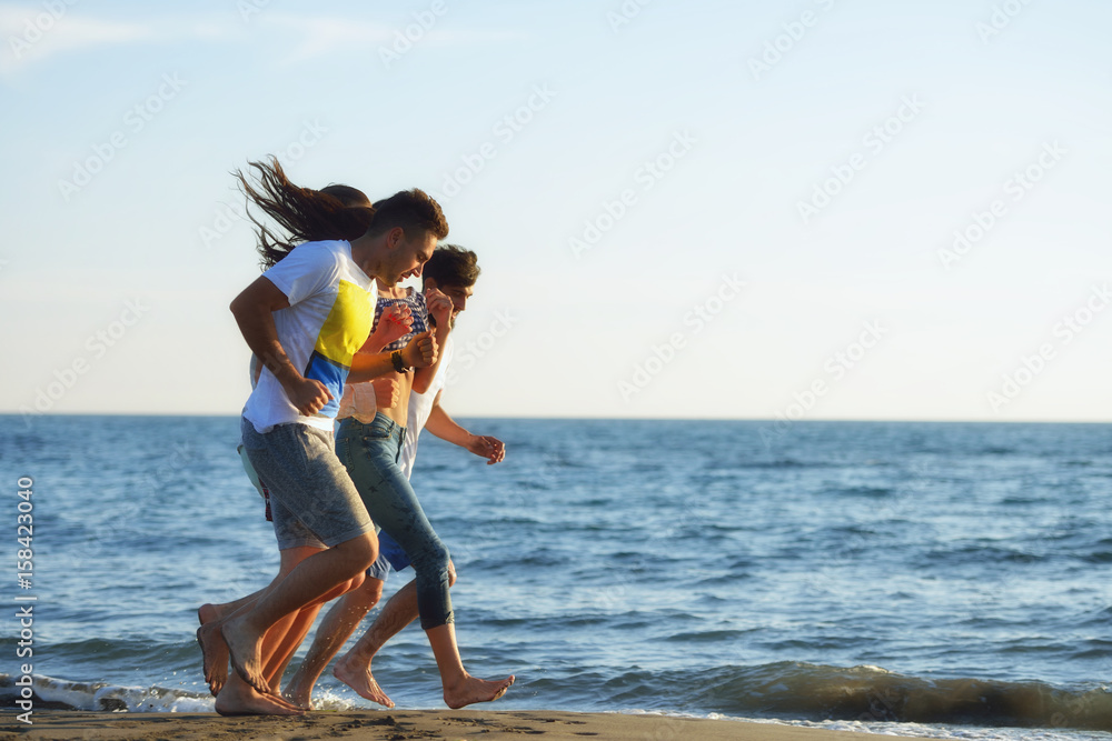 Naklejka premium Group of friends having fun walking down the beach at sunset