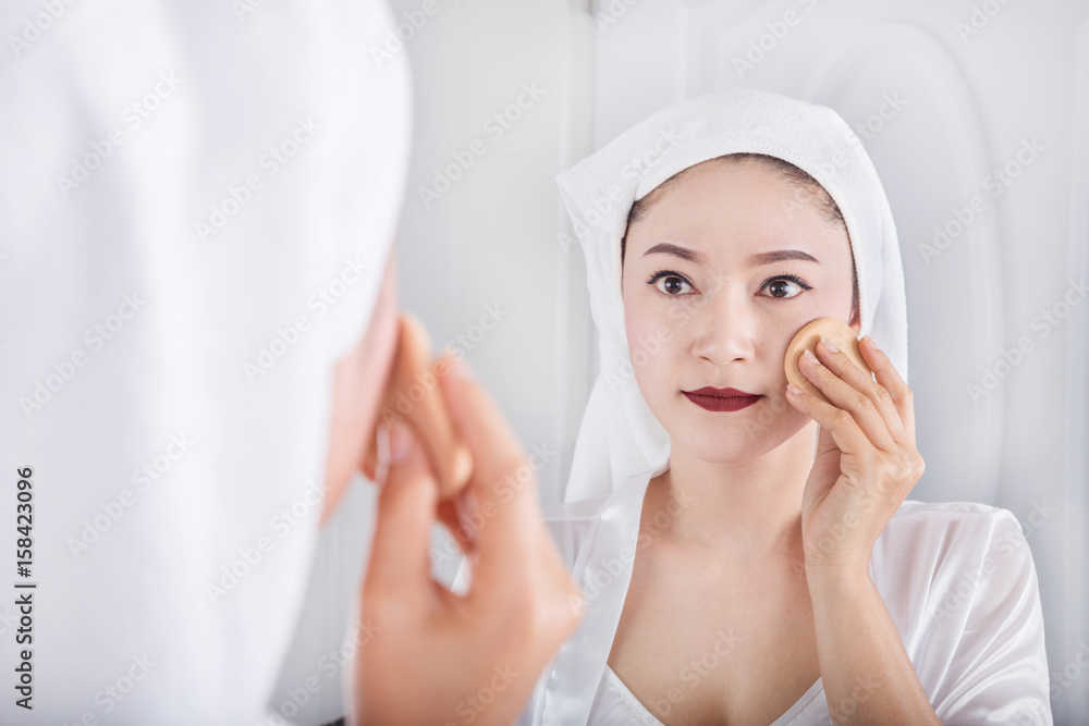 woman looking mirror and applying powder foundation on face woman looking mirror and applying powder foundation on face