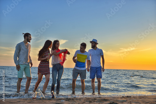 Group of happy young people is running on background of sunset beach and sea