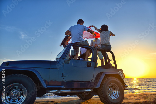 Five young people having fun in convertible car at the beach at sunset.