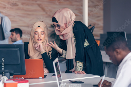 Two woman with hijab working on laptop in office.