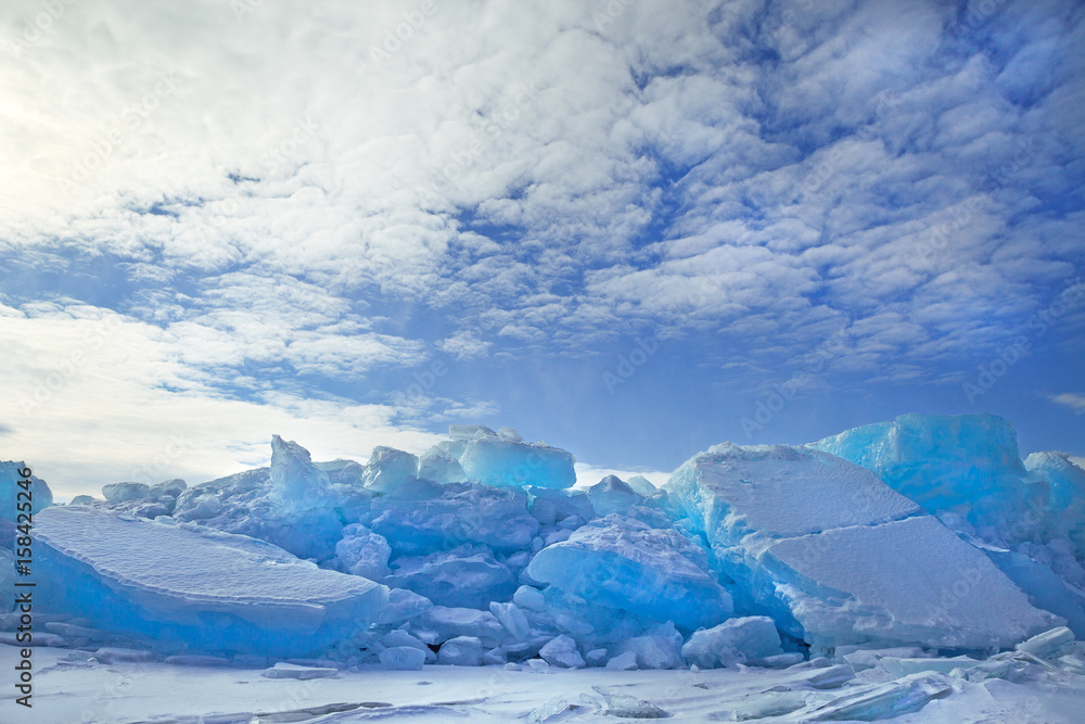 Fototapeta premium Hummocks of turquoise blue ice blocks covered with snow under white clouds