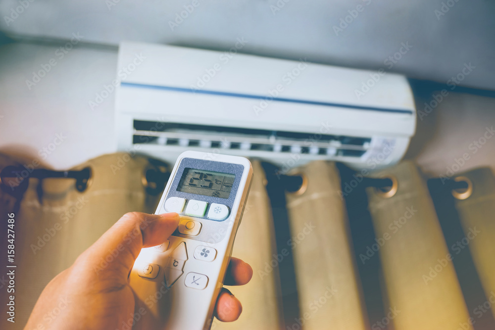 Hand holding the remote control to control the air conditioning Hand holding the remote control to control the air conditioning