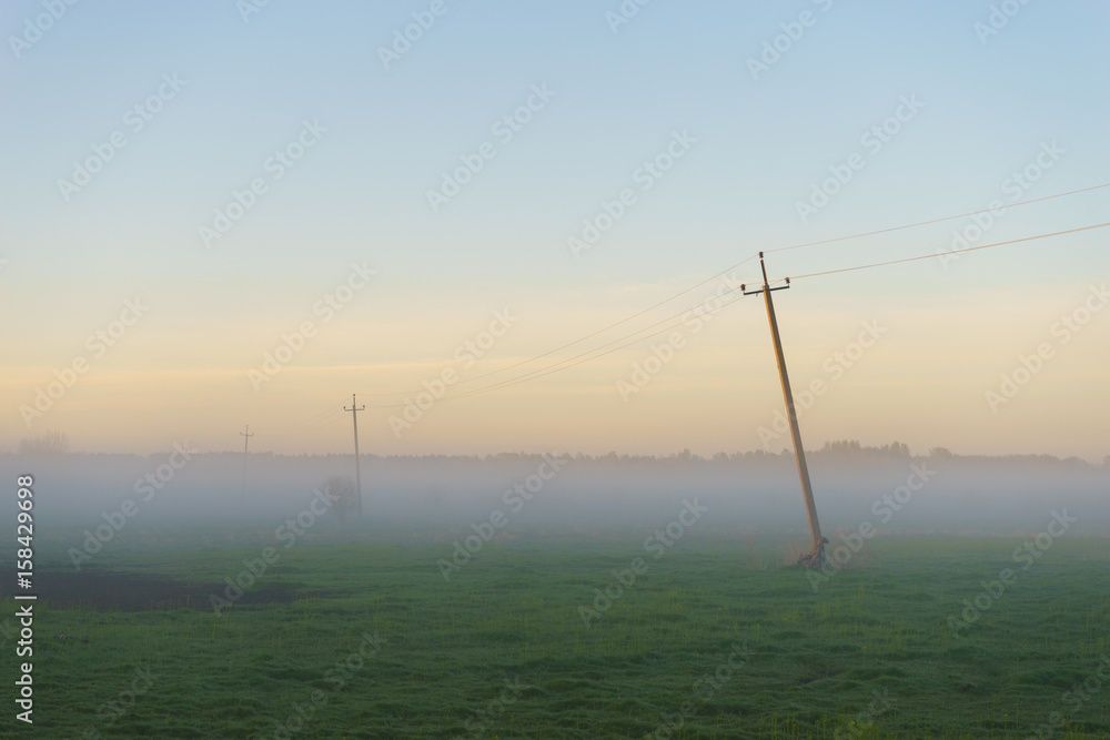 Rural scenery with old power line in thick fog morning