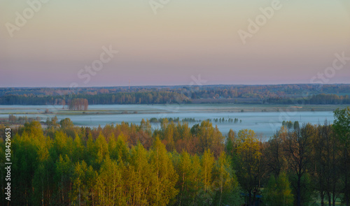 Beautiful sunrise over fields and forests by springtime foggy morning