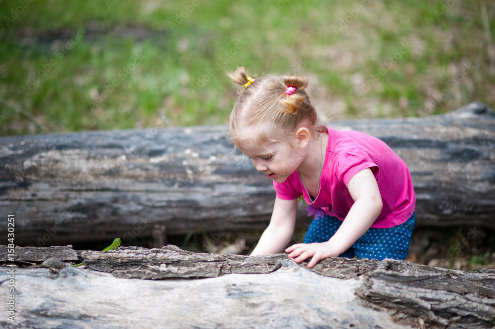 A little girl in a pink T-shirt in the summer for a walk in the clearing. The girl yawns, walks, collects flowers, looks at the lizard. A little girl in a pink T-shirt in the summer for a walk in the clearing. The girl yawns, walks, collects flowers, looks at the lizard.
