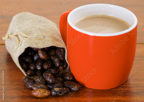 Dry cocoa bean in a small sack and a cup of chocolate over a wooden background photo