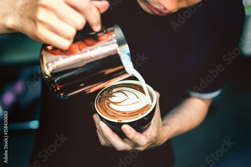 Fototapeta Jak zrobić sztukę latte przez baristę skupioną na mleku i kawie w odcieniu vintage.