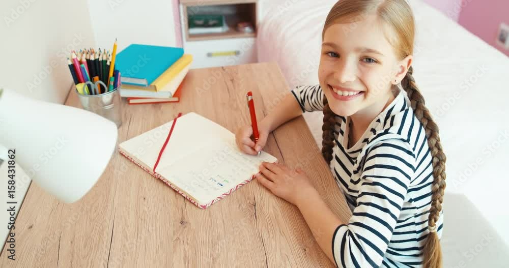 Student girl something writing in exercise book and smiling with teeth at camera. Top view Student girl something writing in exercise book and smiling with teeth at camera. Top view