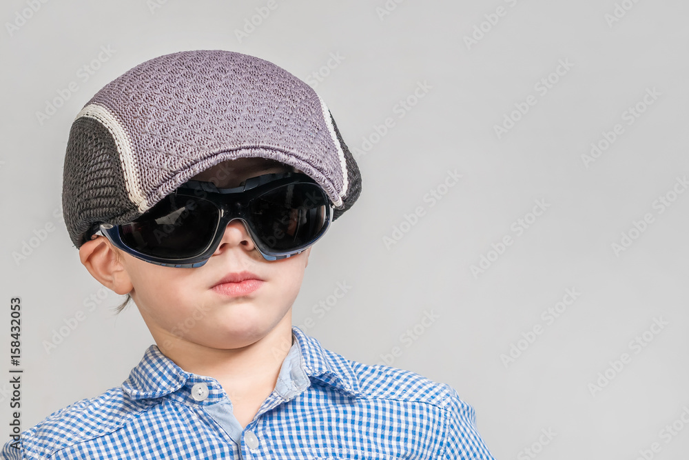 © R - Cute boy in a blue shirt, a cap and sunglasses on a gray background. Isolated