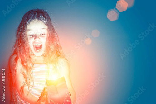 Girl looks in a red glowing gift bag in a dark room