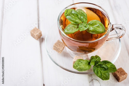 Basil herbal tea in a cup with cane sugar and fresh basil on a white wooden table. Copy space
