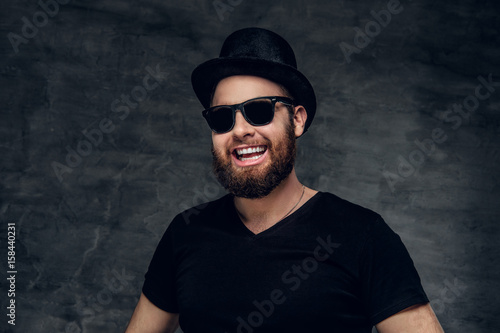 Portrait of bearded male in a black t shirt, cylinder hat and sunglasses.