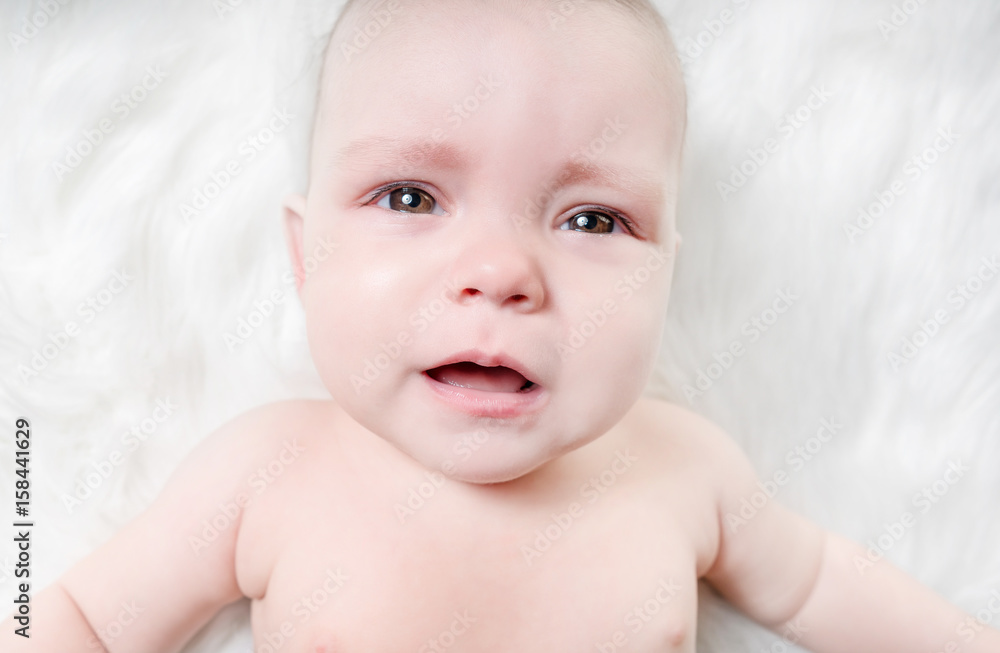Crying baby lies on a white fluffy background Crying baby lies on a white fluffy background