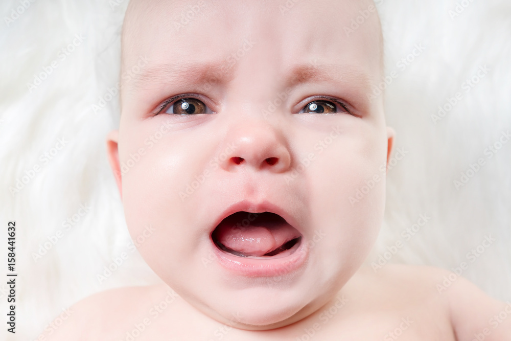 Crying baby lying on a white fur Crying baby lying on a white fur