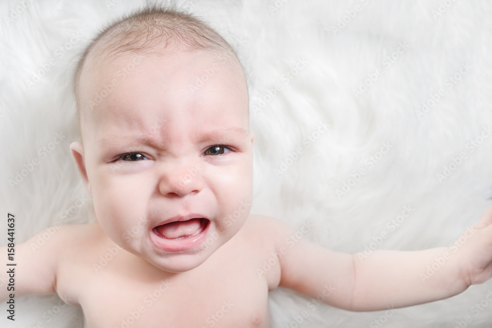 Crying baby lies on a white fluffy background Crying baby lies on a white fluffy background