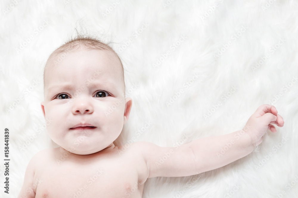 Crying baby lies on a white fluffy background Crying baby lies on a white fluffy background