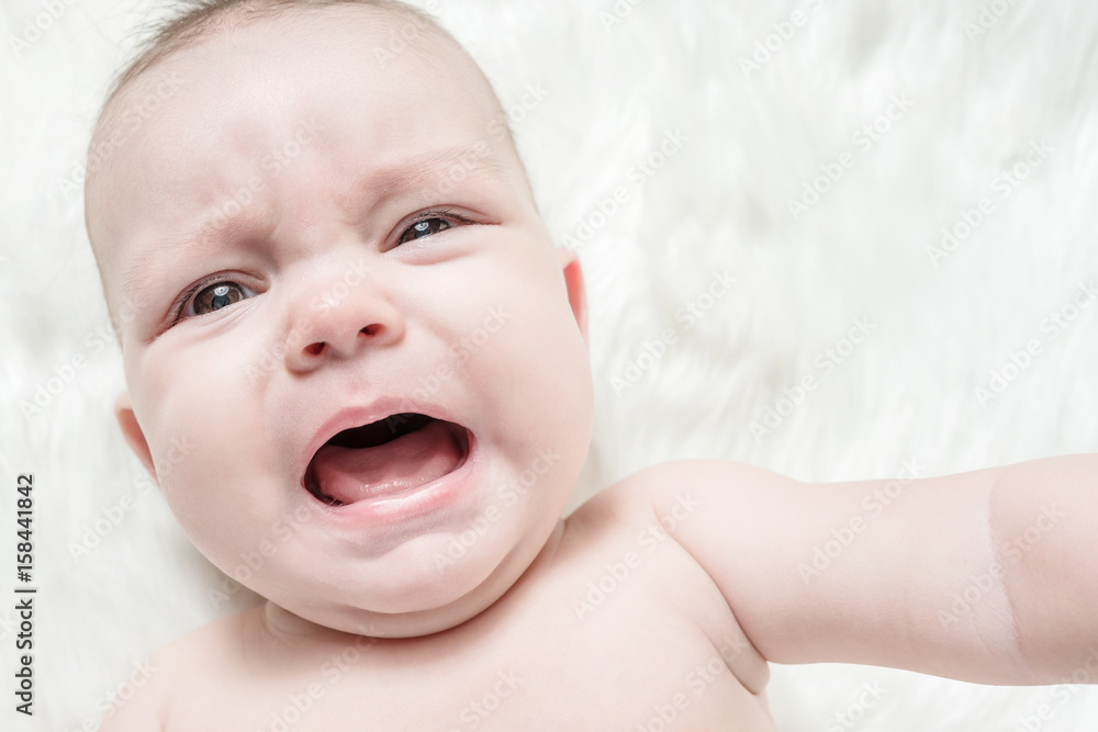 Crying baby lies on a white fluffy background Crying baby lies on a white fluffy background