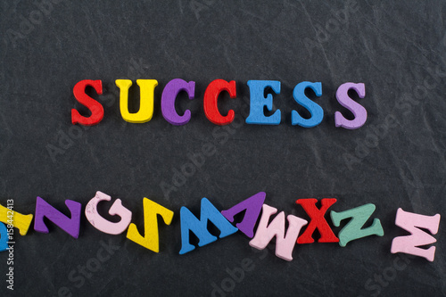 SUCCESS word on black board background composed from colorful abc alphabet block wooden letters, copy space for ad text. Learning english concept.
