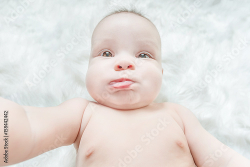 Cute baby lying on a white fur with a funny grimace on his face