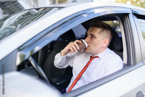 Businessman eating a burger and drink coffee in the car.