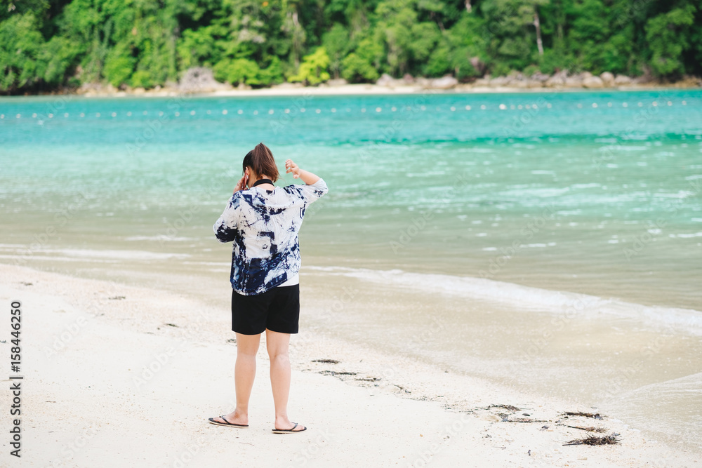 asia woman talking with phone and walking around sand beach. have sea and forest are background. this image for people,nature,seascape and technology concept